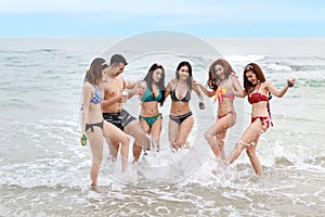 Group of happy young asian women and man wearing bikini or swimming suit. They kicking water, holding alcohol and soft drink