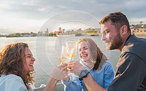 Group of happy young friends enjoying  boat trip  at sunset drinking wine and celebrating