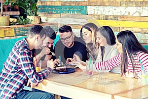 Group of happy young friends sharing and eating dessert cake at cafe table