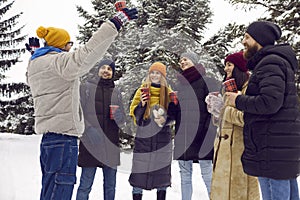 Group of happy young men and women drinking coffee and having fun in winter park