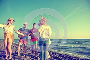 group of happy young people dancing at the beach on beautiful summer sunset