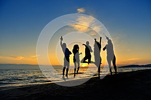 Group of happy young people dancing at the beach on beautiful summer sunset