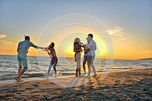 Group of happy young people dancing at the beach on beautiful summer sunset