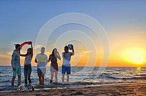 Group of happy young people dancing at the beach on beautiful summer sunset