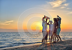 Group of happy young people dancing at the beach on beautiful summer sunset