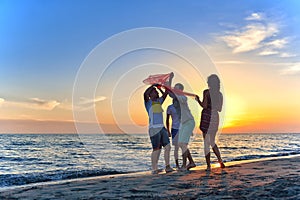 Group of happy young people dancing at the beach on beautiful summer sunset