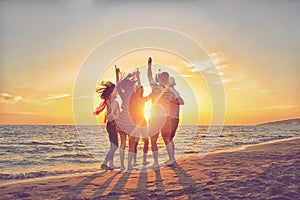 Group of happy young people dancing at the beach on beautiful summer sunset
