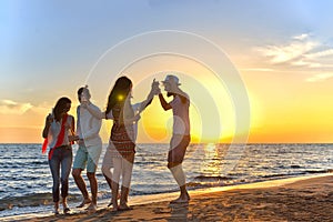 Group of happy young people dancing at the beach on beautiful summer sunset