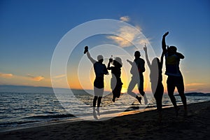Group of happy young people dancing at the beach on beautiful summer sunset