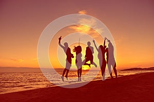 Group of happy young people dancing at the beach on beautiful summer sunset