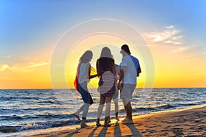 Group of happy young people dancing at the beach on beautiful summer sunset