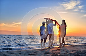 Group of happy young people dancing at the beach on beautiful summer sunset