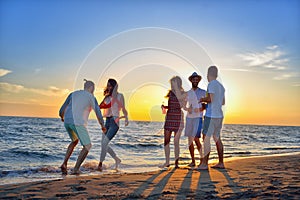 Group of happy young people dancing at the beach on beautiful summer sunset