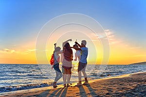 Group of happy young people dancing at the beach on beautiful summer sunset