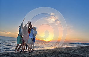 Group of happy young people dancing at the beach on beautiful summer sunset