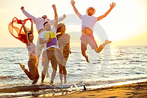 Group of happy young people dancing at the beach on beautiful summer sunset