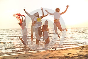 Group of happy young people dancing at the beach on beautiful summer sunset