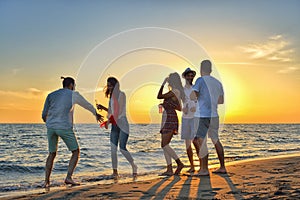 Group of happy young people dancing at the beach on beautiful summer sunset