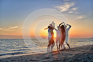 Group of happy young people dancing at the beach on beautiful summer sunset