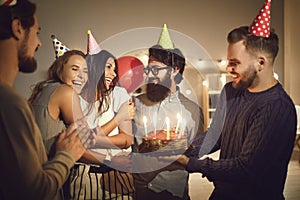 Group of happy young people giving delicious cake to their friend for her birthday