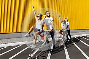 A group of happy young people, having fun on shopping carts, ride on a shopping cart. summer day with sunlight