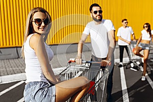 A group of happy young people, having fun on shopping carts, ride on a shopping cart. summer day with sunlight