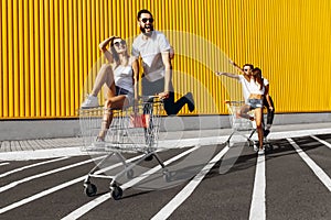 A group of happy young people, having fun on shopping carts, ride on a shopping cart. summer day with sunlight