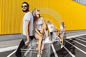 A group of happy young people, having fun on shopping carts, ride on a shopping cart. summer day with sunlight