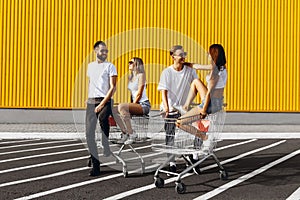 A group of happy young people, having fun on shopping carts, ride on a shopping cart. summer day with sunlight