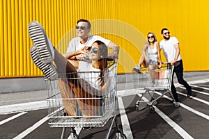 A group of happy young people, having fun on shopping carts, ride on a shopping cart. summer day with sunlight
