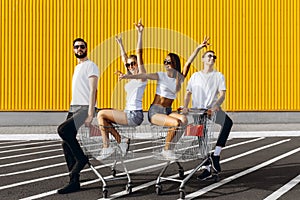 A group of happy young people, having fun on shopping carts, ride on a shopping cart. summer day with sunlight