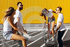 A group of happy young people, having fun on shopping carts, ride on a shopping cart. summer day with sunlight