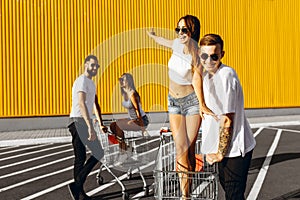 A group of happy young people, having fun on shopping carts, ride on a shopping cart. summer day with sunlight