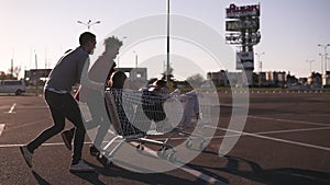 Group of happy young people having fun on shopping trolleys. Multiethnic young people racing on shopping cart. Beautiful