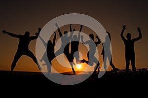 Group of happy young people silhouettes jumping on the beach  on beautiful summer sunset