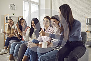 Group of happy young women sitting on sofa, drinking coffee, chatting and laughing