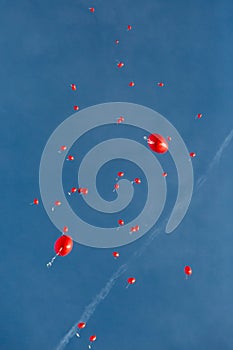 Group of heart-shaped red balloons flying in blue sky