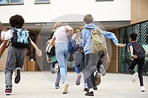 Group Of High School Students Running Into School Building At Beginning Of Class