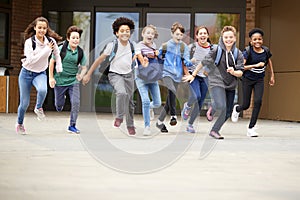 Group Of High School Students Running Out Of School Buildings Towards Camera At The End Of Class