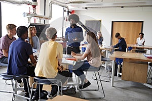 Group Of High School Students Sitting At Work Benches Listening To Teacher In Design And Technology Lesson