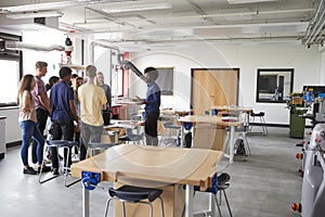 Group Of High School Students Standing Around Work Bench Listening To Teacher In Design And Technology Lesson