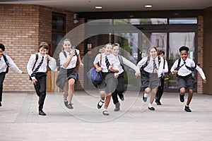 Group Of High School Students Wearing Uniform Running Out Of School Buildings Towards Camera At The End Of Class