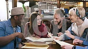 Group of hipster friends reading menu and choosing dishes in the bar, pub.