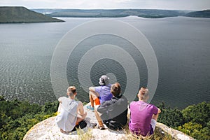 Group of hipster travelers sitting on top of rock mountain and enjoying  amazing view on river. Young guys explorers relaxing and