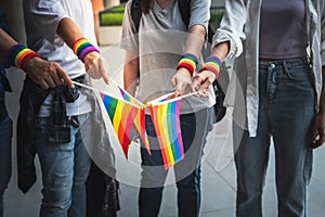 A group of homosexual people wearing their wrists and holding a flag showing the LGBT symbol