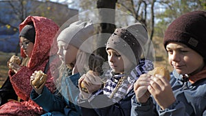 Group of hungry kids are eating burger outdoor in the park in sunny autumn day