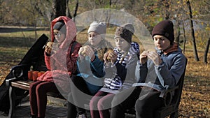 Group of hungry kids are eating burger outdoor in the park in sunny autumn day