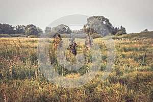 Group of hunters crossing through tall grass in rural field at dawn during hunting season