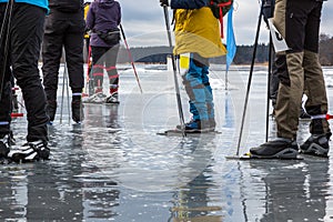 Group of ice skaters on wet melting ice on frozen lake taking a break. Late winter daytime in Sweden.