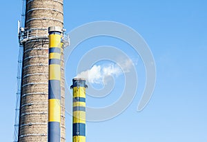 Group of industrial chimneys with smoke against blue sky